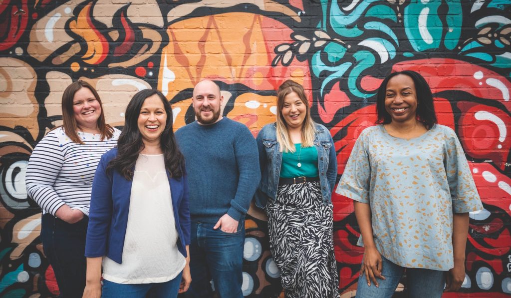 Gritty Talent team - a diverse group of people in gront of a graffiti wall