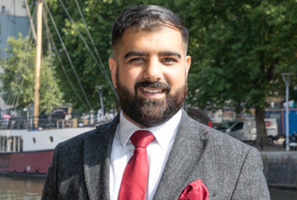 Ali Kazmi, Founder of Ethical Equitym, smiling in a suit at Bristol's harbour
