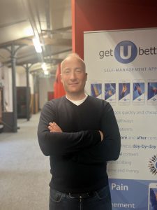 Dr Carey McClellan in SETsquared Bristol office space with getUBetter banner