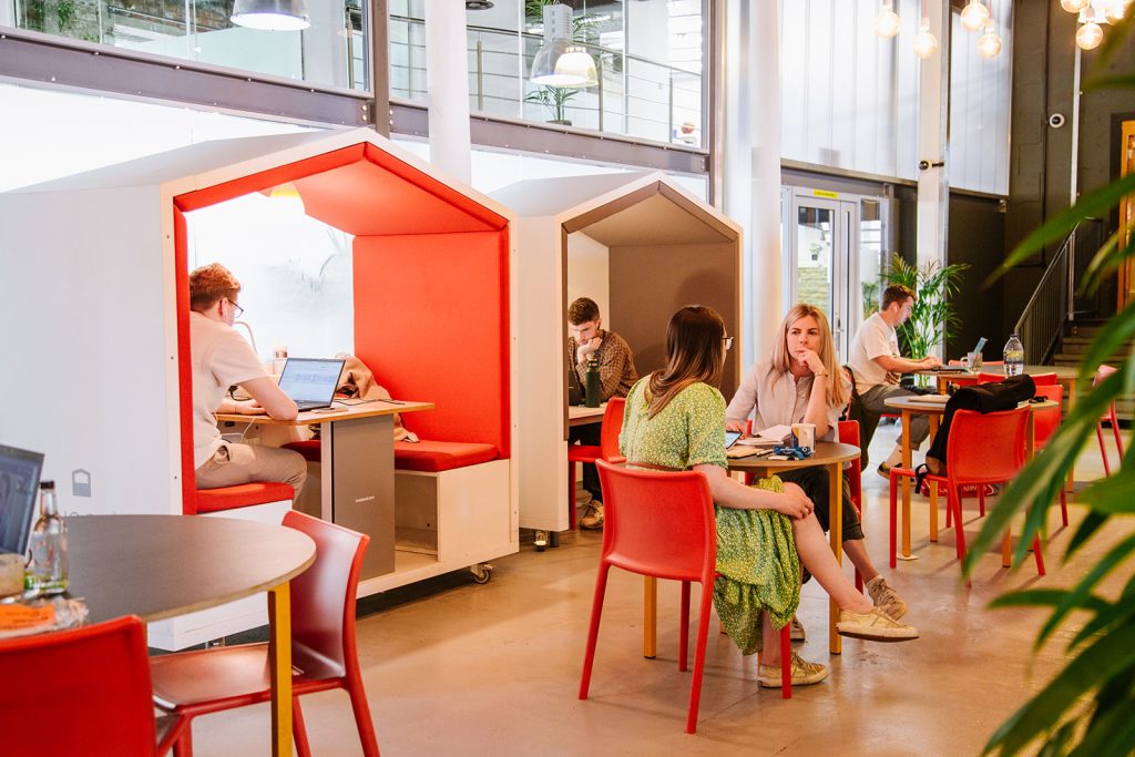People working in Engine Shed members lounge, a colourful, space with contemporary designed and workspaces and plants