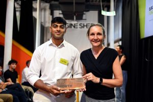 A man in a white shirt and name badge saying EarTide receiving an award from a woman in a black top.