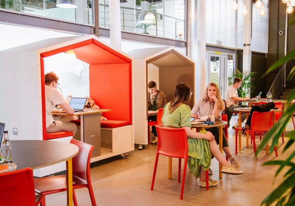 People working in Engine Shed members lounge, a colourful, space with contemporary designed and workspaces and plants